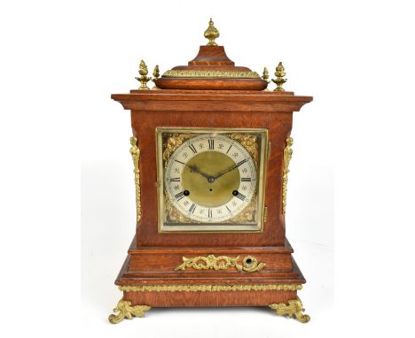 A 19th century oak cased German mantel clock, with applied brass urn surmounts and beaded decoration surrounding the square f