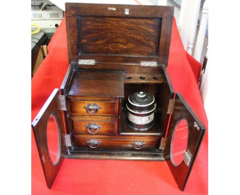 An Edwardian oak smokers cabinet, two doors open to reveal fitted interior of drawers and a tobacco jar, 32cm wide