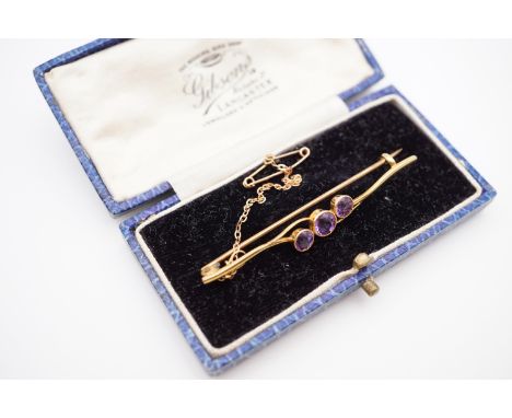 An antique yellow-metal and amethyst bar brooch, having three round-cut amethysts, millegrain set to the centre of a cleft an