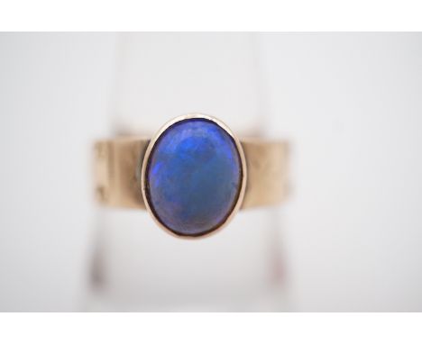 A late Victorian Arts and Crafts opal cabochon ring, of approximately .78ct, bezel set above a decoratively punched and engra