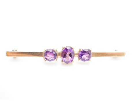 A vintage 9ct gold and amethyst bar brooch, with central oval cut and claw-set amethyst of approximately .85ct, flanked by a 