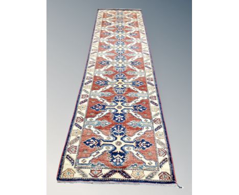 An Afghan/Caucasian design runner, the deep brick red field with a single column of medallions enclosed by ivory slant leaf b