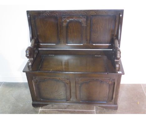 A darkwood carved and panelled monks bench with crouching lion arm rests and hinged seat with storage below - height of back 