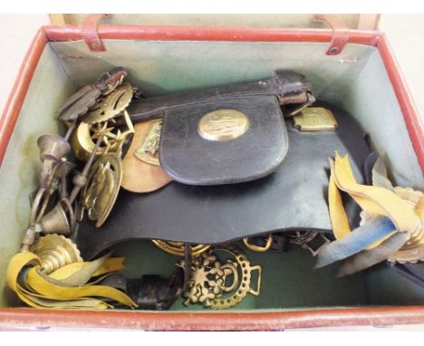 A case containing vintage horse brasses, some on old harness, a bit and a crotal bell