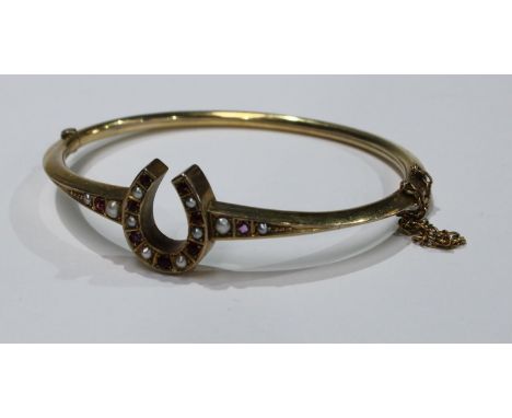 A gold hinged bangle, the centre as a horse shoe set with seed pearls and ruby chips, unmarked, 8.4g 