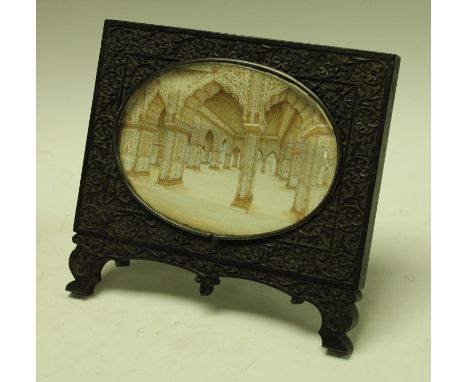 A 19th century Indian carved ebony easel frame set with an oval minitature on ivory depicting a white marble interior possibl