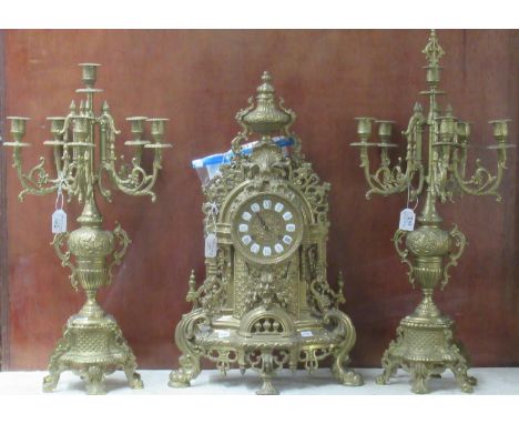 Victorian style brass clock garniture set, the two train clock with mask head and urn decoration, flanked by two candelabras.