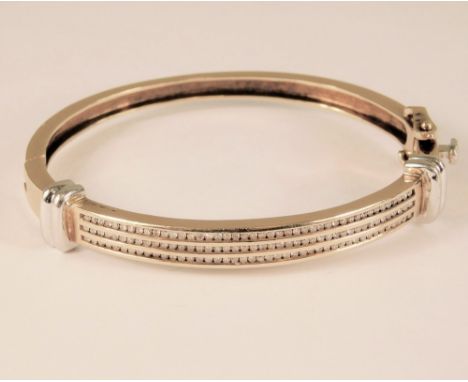 GOLD BANGLE.A 9k bangle in yellow & white gold, the front set with three rows of small brilliant cut diamonds, totalling appr
