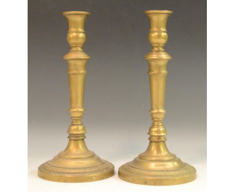 A pair of French Empire brass candlesticks, campana sconces, knopped stems, circular bases with engine turned borders, 26.5cm