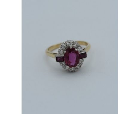 A ruby and diamond ring, the principal oval cut stone with baguette shoulders, claw mounted within a border of diamonds to an