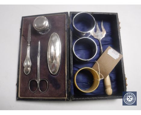 A cased silver four piece nail kit, a silver pronged fork, two silver napkin rings, Bakelite napkin ring with silver badge 