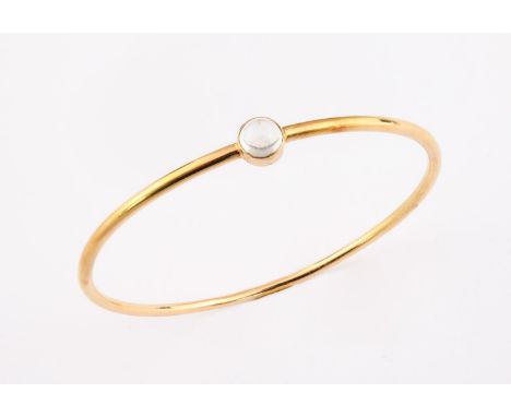 AN 18CT GOLD BANGLE mounted with a circular cabochon moonstone, internal measurements 7.0cm dia., 25 grams