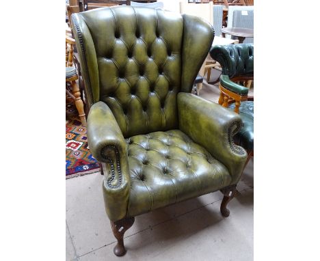 A green button back upholstered wing armchair on carved cabriole legs.