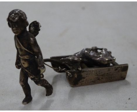 A small silver figure of a cherub and sled