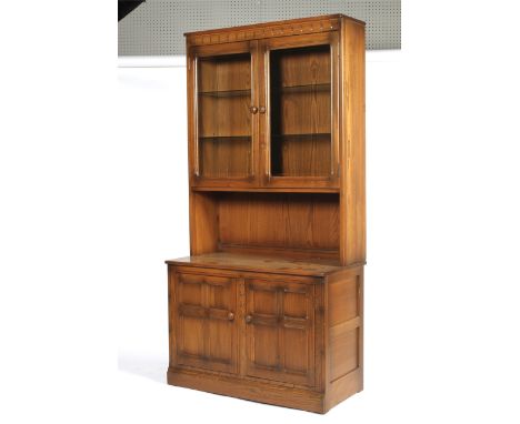 An Ercol oak dresser. The glazed double doors enclosing a shelf, electrified, with turned wooden handles, the base with panel