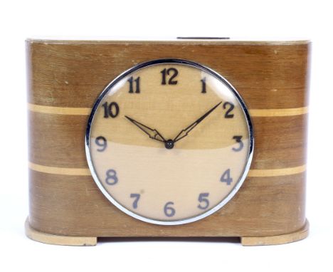 An Art Deco wooden cased mantle clock. Of unusual form, the central face with black numerals set in a curved frame. Incorpora