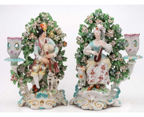 A pair of Derby porcelain figural candlesticks: modelled as a shepherd and companion, he standing cross legged playing the ba