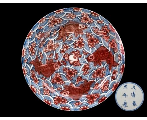 A Chinese underglaze blue and copper-red charger: boldly painted with four carp swimming amongst lotus blooms on a wave groun