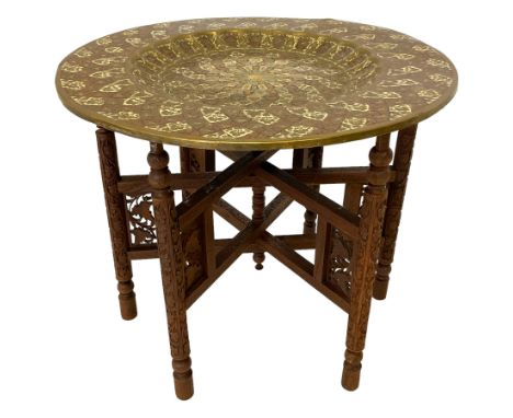Early 20th century Benares folding table, the circular brass dished top with embossed enamel work, on profusely carved foldin