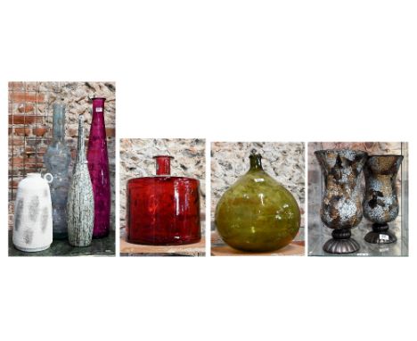A red glass carboy of cylindrical form, a green glass carboy, two tall glass vases, a ceramic vase with loop handle and three