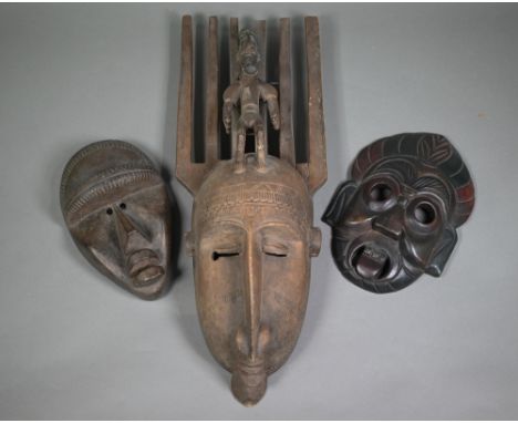 A Bambara (Mali) carved wood mask with six-tooth 'comb' top supporting a male figure with pipe, 64 cm high, to/w two other ma