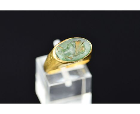 A ROMAN GOLD AND GREEN GLASS INTAGLIO SEAL RING, possibly 4th or 5th Century A.D., the oval intaglio carved with a profile po
