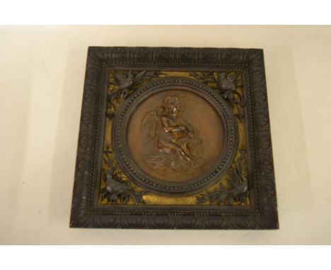 Italian circular carved walnut panel of a seated cherub holding an arrow in a square frame with carved bird decoration, inscr