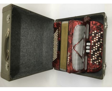 A cased Hohner Riviera II accordion in a marbled red finish.