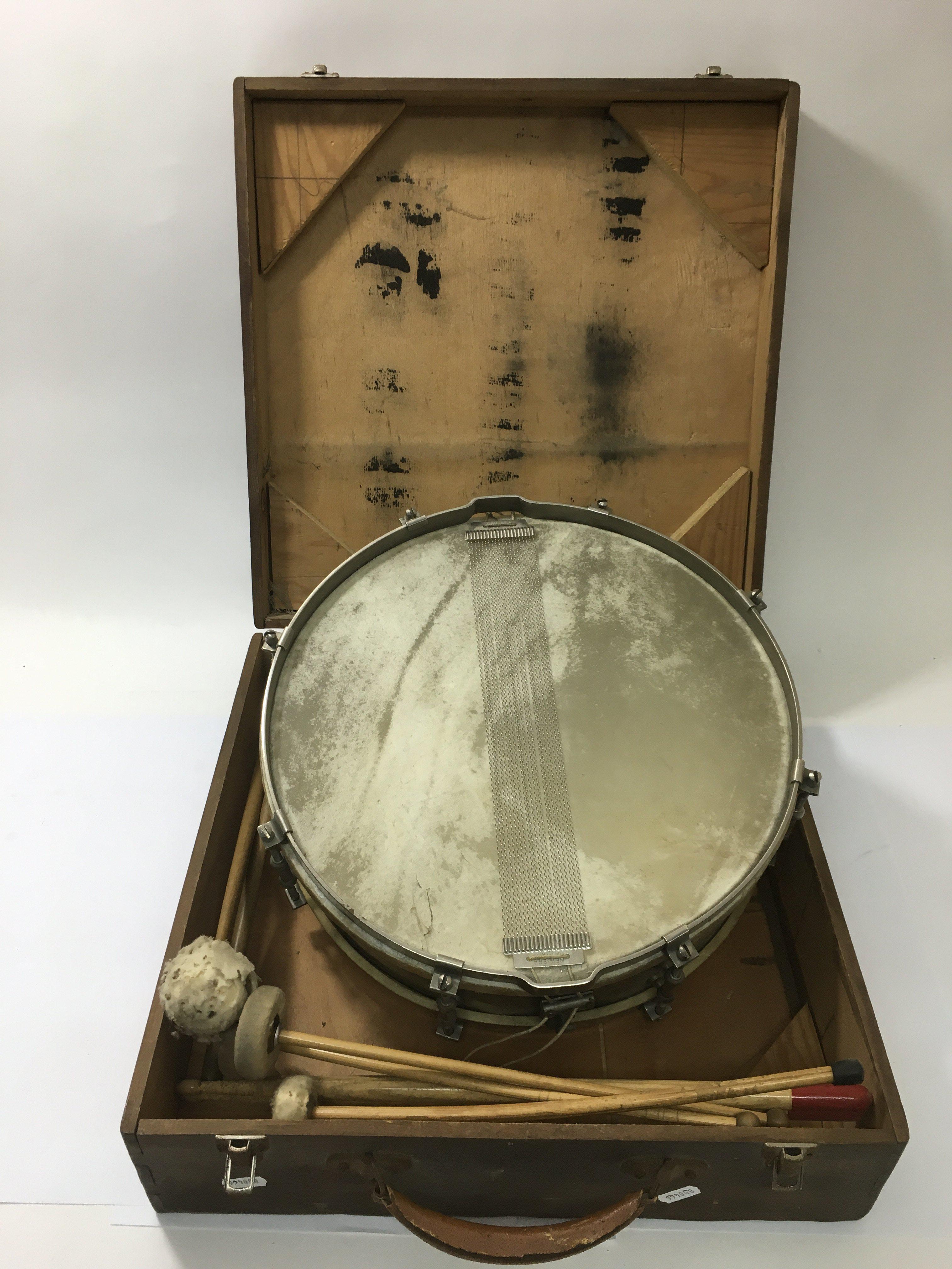 A vintage John Grey snare drum in a wooden case with various drumsticks.