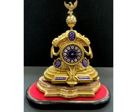 A gilt mteal mantel clock under a glass dome, eagle and globe finial, blue enamelled face, Roman numerals. 45cm high.