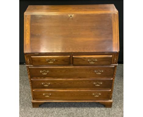 A 20th century Reprodux oak bureau, fall front enclosing pigeonholes, a small door, two short drawers above two short drawers