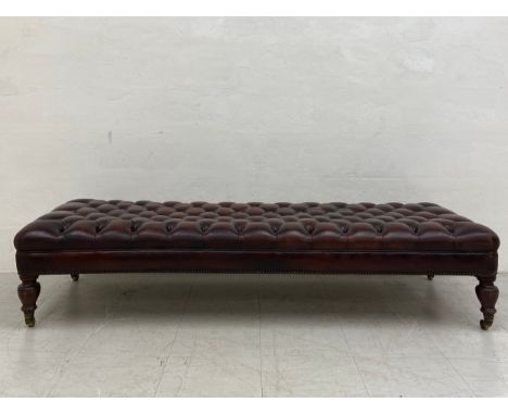 A large late 19th century ottoman or footstool having a deep buttoned brown leather seat raised on four turned cup and cover 