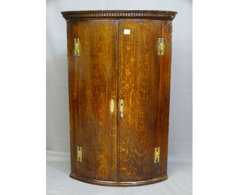 AN OAK HANGING CORNER CUPBOARD, two door, bow fronted with brass H hinges, dentil cornice and three bow fronted interior shel