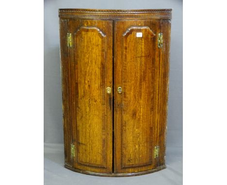 A 19TH CENTURY TWO DOOR OAK BOW FRONTED HANGING CORNER CUPBOARD, each door having applied cross banded panels with brass H hi