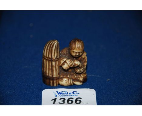 An Edo period (1605-1860) Netsuke, carved from a single piece of Ivory, in the form of a seated figure next to a bundle of st