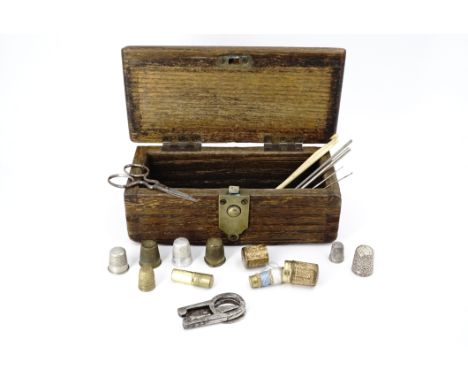 An antique wooden box containing a quantity of sewing tools, including two silver thimbles, and a sewing etui