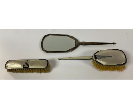 An Art Deco George V silver three piece hand brush and mirror set, the monochrome engine turned enamel applied with a skyscra