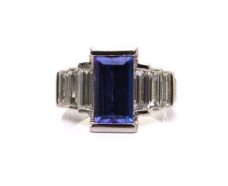 An Art Deco-style platinum tanzanite and diamond ring, featuring a tapered rectangular step-cut tanzanite, approximately meas