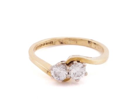 A two stone diamond crossover ring; the round brilliant cut diamonds in claw mount to a cross-over 18 carat gold setting and 