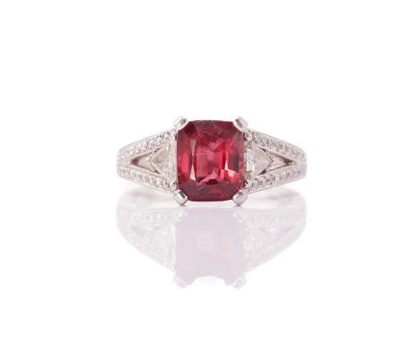 A red spinel and diamond ring in platinum, consisting of a cushion-cut spinel claw set in the centre, flanked by two triangul