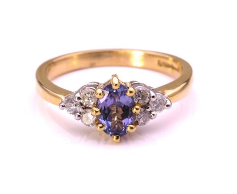 A tanzanite and diamond ring in 18ct gold, containing an oval-cut tanzanite approximately measures 7.0 x 5.0 mm, flanked by d