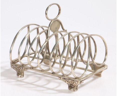 George IV silver toast rack, London 1824, maker WE, the oval loop carrying handle above an oval vacant cartouche and six scro