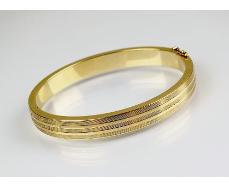 A yellow metal hinged bangle, with reeded engine turned decoration, the clasp stamped '585', with attached safety catch, weig