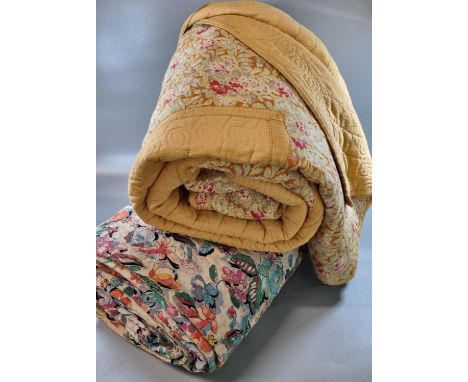 Two vintage quilts; one with a floral print and the other a cotton patchwork on a mustard ground with floral print and plain 