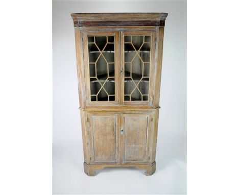A large stripped limed oak two sectional corner cupboard, the twin panelled Astragal glazed doors revealing a shelved interio