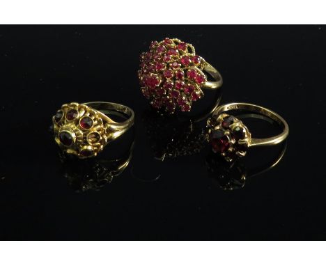 A ruby set cocktail ring of tiered form, 9ct gold garnet daisy ring and a garnet set ring stamped 585 (one stone missing) (3)