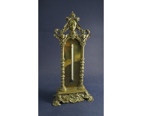 An ornate brass desk thermometer with cherubic masks, 23cm tall 