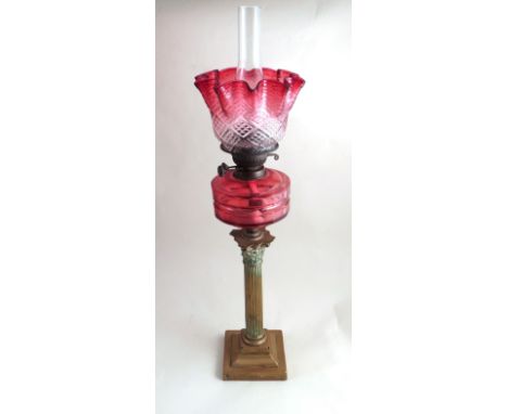 A Victorian oil lamp with tinted cranberry glass shade, faceted reservoir over brass Corinthian column on a stepped base.  Wo
