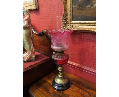 A Victorian cranberry glass oil lamp with swag etched shade over brass base 
