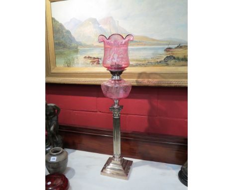 A Victorian Cranberry glass oil lamp, floral glass shade and reservoir above a silver plate Corinthian column with stepped ba